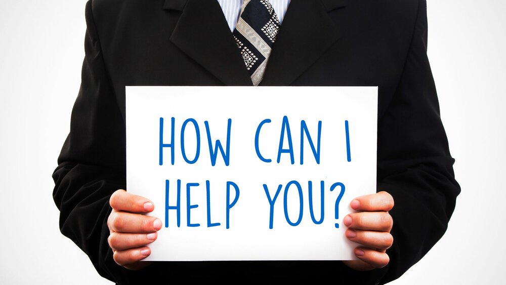 A professional holding a sign that reads How can I help you?